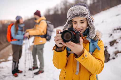 Boy photographing using dslr camera while parents are discussing in the background on winter hiking tour