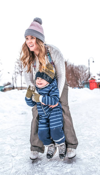 mulher no inverno com seu filho, um garotinho 3-5 anos de idade, treinar e aprender a patinar, em roupas quentes, sorrindo feliz, relaxar no fim de semana. a neve do fundo drifts a pista de gelo. emoções de alegria e riso. - baby goods flash - fotografias e filmes do acervo