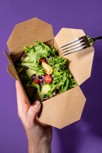 Woman's hand holds a mixed salad in cardbox with fork other hand. stock photo
