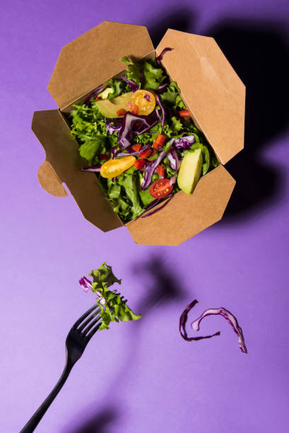 Mixed salad in cardbox on purple background with fork. stock photo