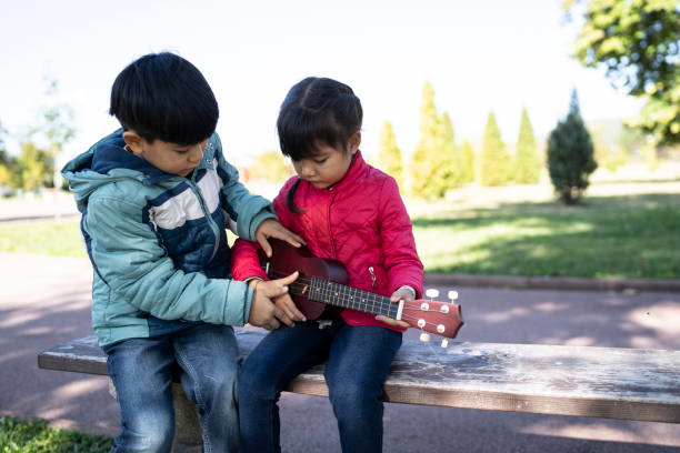 istock Little boys sitting on bench in park and playing a guitar 1182403148