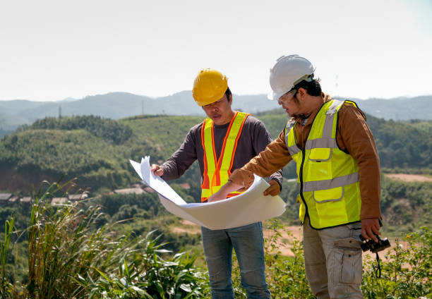 istock Engineer manager man discuss with his team who hold construction plan and stay in front of mountain view and  high voltage pole 1182409194