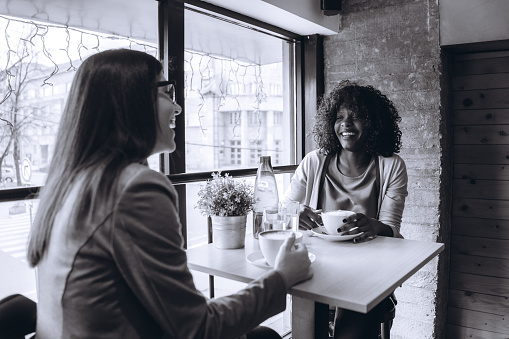 Two young multi-ethnic women drinking coffee in cafe.