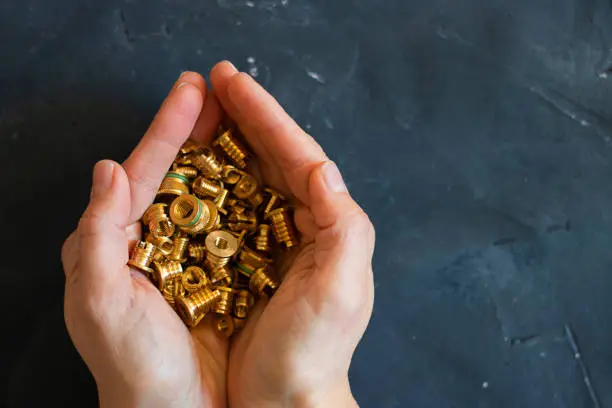 Handful of gold Pop rivet nuts ond lochnuts in human hands on black tectured chalk board surface. Close up. Fasteners, screws and details. Top view. Horizontal with copy space.