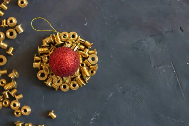 Round form made of gold pop rivet nuts ond lochnuts with red christmas ball on it on black tectured chalk board. Horizontal copy space. New year concept. Fasteners, screws and details. Top view.