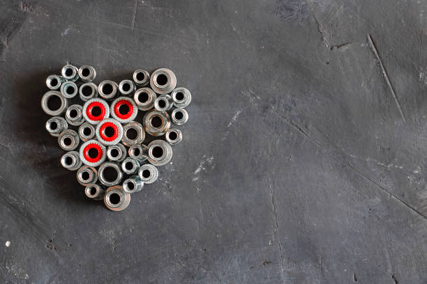 Horizontal frame made of pop rivet nuts and locknuts with red plastic, stainless steel mandrel on black tectured chalk board surface. Fasteners, dtails. Copy space. Top view. St. Valentine's day corazón hecho de tuercas de remache pop y tuercas de acero con plástico rojo, mandril de acero inoxidable sobre la superficie de la tabla de tiza tectured negro. blanco y negro. fijaciones, tornillos, detalles. vista superior. día de san valentín
