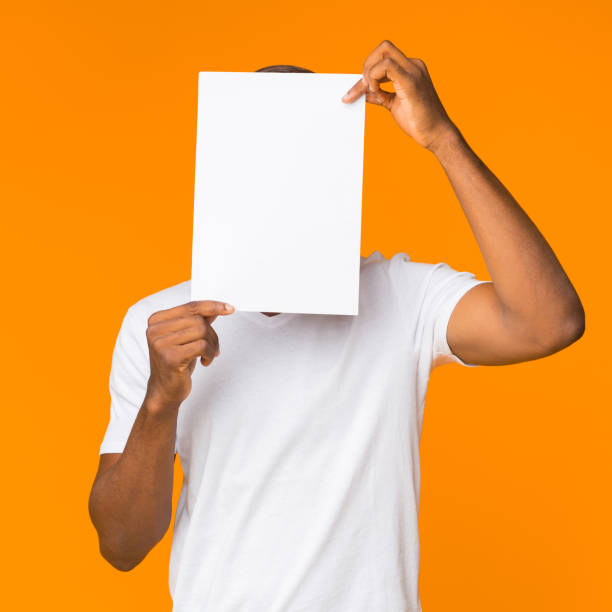 istock Black Man Covering Face With Paper Sheet Standing, Orange Background 1182415815