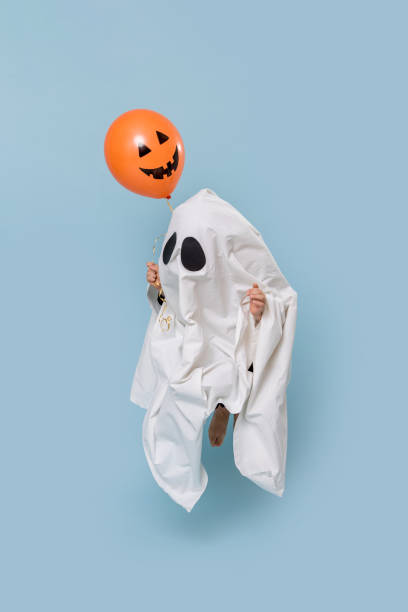 kleines kind als weißer geist auf halloween schwebend in der luft über blau - child jumping vegetable food stock-fotos und bilder