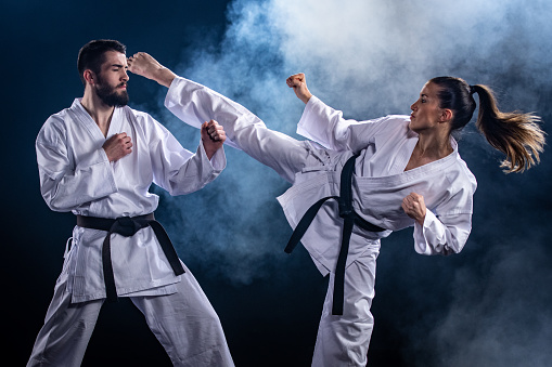 Male and female karate players fighting during competition against blue background.
