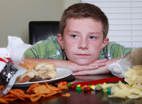 Boy leans his head down with a sad and tired expression while surrounded by junk food