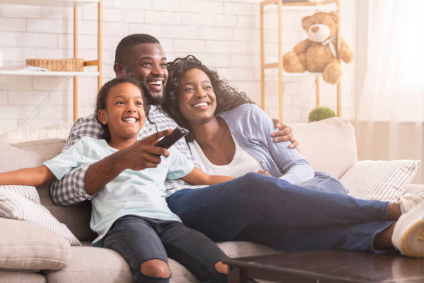 Happy black family relaxing and watching tv at home Happy african american family relaxing and watching tv at home, enjoying weekend together. watching tv stock pictures, royalty-free photos & images