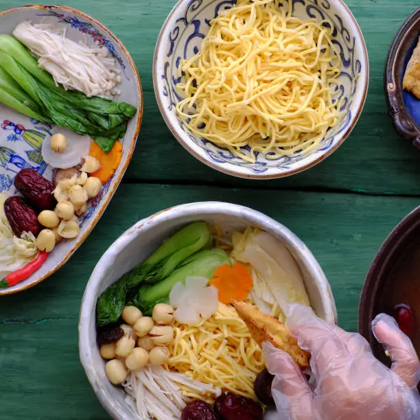 People prepare Vietnamese vegetarian homemade noodle soup bowl from vegan ingredient for breakfast, healthy dish from tofu, jujube fruit, lotus seed, bok choy, mushroom, spice, carrot
