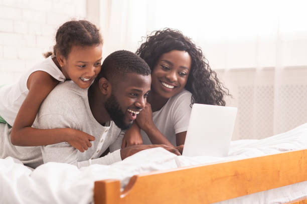 istock African family lying on bed browsing internet on laptop together 1182427685