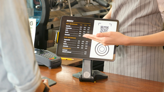 Close up of waitress hand showing coffee menu on digital tablet  to customer for ordering at counter coffee shop, small business food and drink concept
