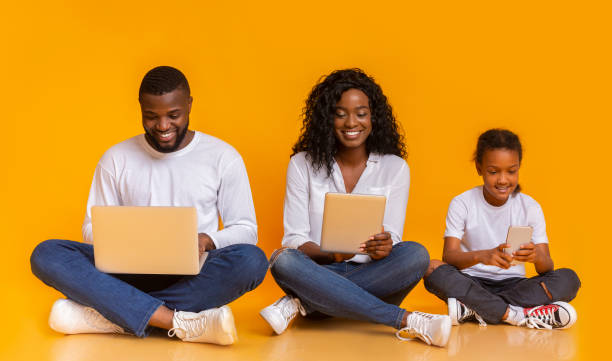 istock Happy black family using different gadgets, sitting on floor together 1182428030