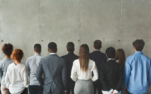 Businesspeople looking at grey wall with free space, standing in row, back view