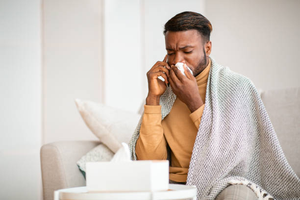 istock Afro Guy Blowing Nose In Napkin Sitting On Sofa Indoor 1182430336
