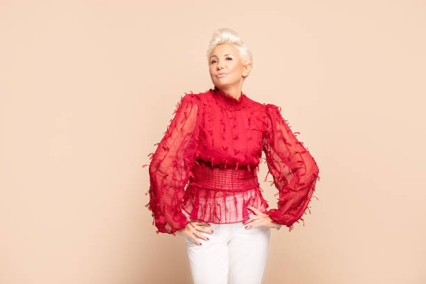 Elegant adult lady in red fashionable shirt. Fashion portrait of adult woman with short blond hair posing in red elegant shirt over beige background in studio. Middle age lady in glamour makeup. middle aged woman fashion stock pictures, royalty-free photos & images