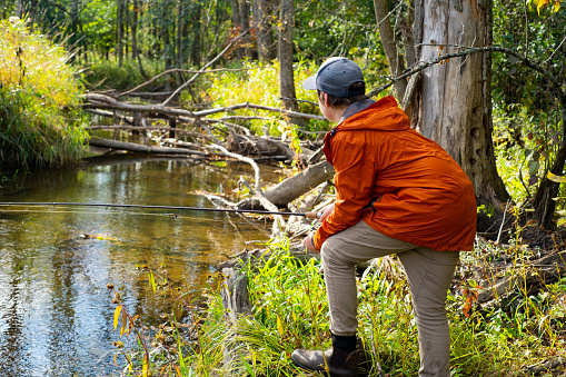 A young fisherman looks out on a small trout stream in late afternoon light.