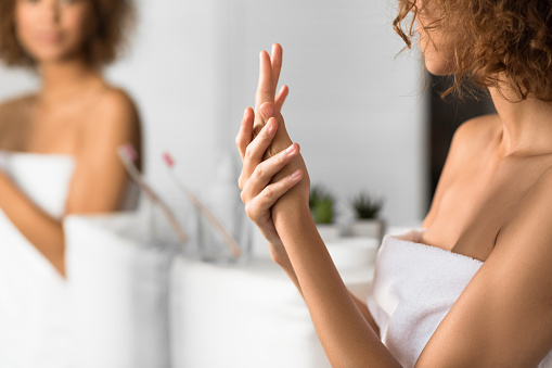 Mujer irreconocible aplicando crema de manos en el baño photo