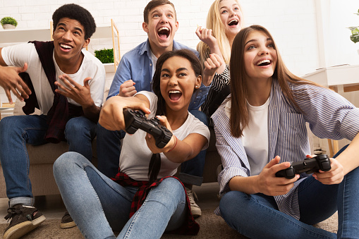 Overjoyed teen friends playing video games, having fun together at home