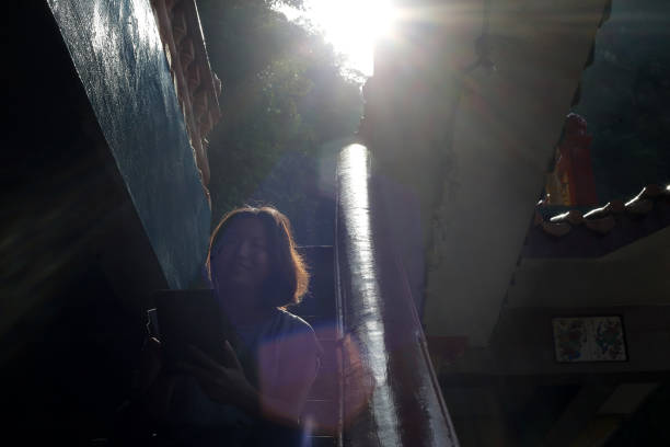 A female adult is sitting on staircase while holding digital tablet cheerfully at Chinese temple in Ipoh, Perak Malaysia.