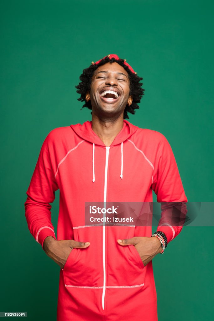Funny christmas portrait of happy young man wearing in red pajamas Funny Christmas portrait of young afro American man wearing red onesies, looking up and laughing. Studio shot against green background. 25-29 Years Stock Photo