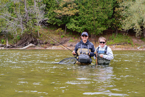 Two fishing brothers, wearing waders standing in a trout stream holding fishing rods.