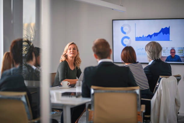 Businesswoman Listening to Associate During Video Conference Rear view personal perspective of diverse executive team video conferencing with male CEO and discussing data. meeting room stock pictures, royalty-free photos & images