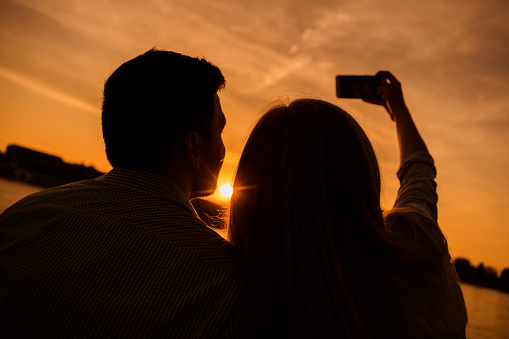 Happy couple is taking selfie in sunset in the city.