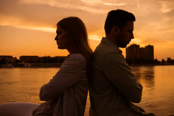 junges paar bei sonnenuntergang - rücken an rücken stock-fotos und bilder