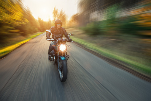 Motorcycle driver riding in forest landscape with blurred motion effect of surrounding background.