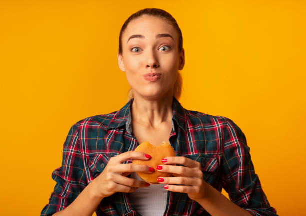 istock Girl Eating Burger Having Cheat Meal Standing On Yellow Background 1182442169