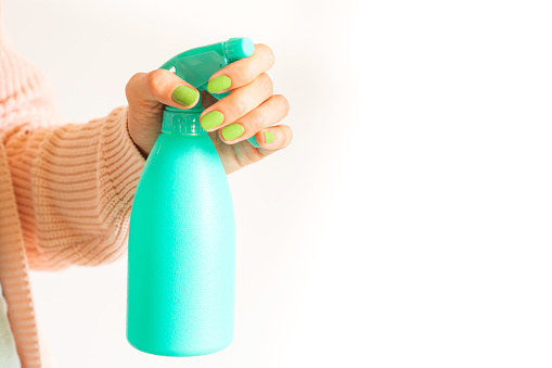 Woman's hand holding mint green spray bottle with home made detergent. Natural products for cleaning or body care concept