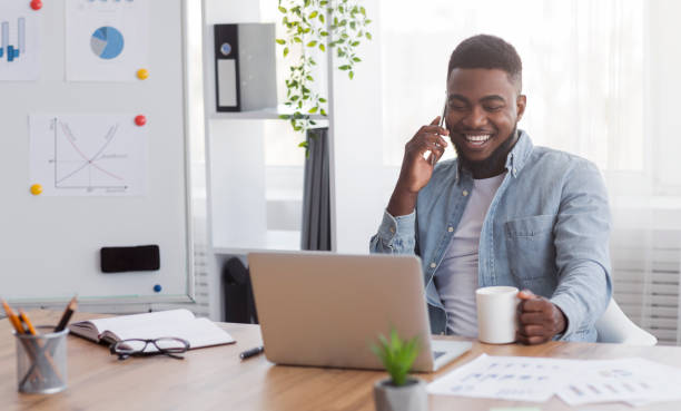 istock Cheerful black manager talking on mobile phone and drinking coffee 1182445969