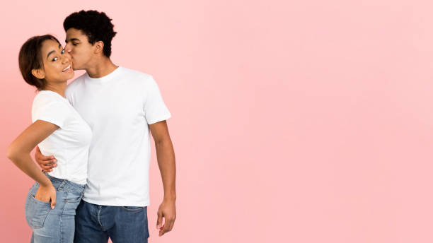 istock Afro guy kissing girlfriend in cheek, pink background 1182445986