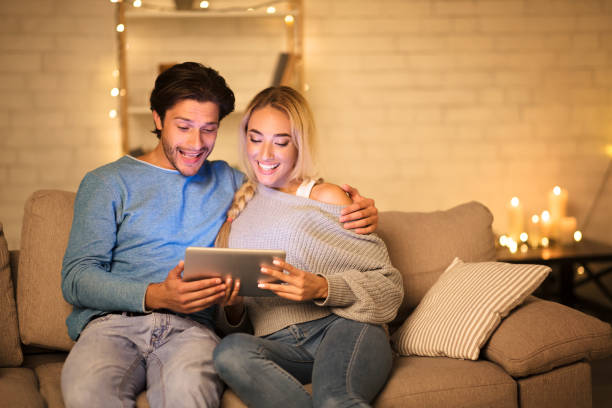 istock Excited couple using digital tablet in cozy living room 1182446082