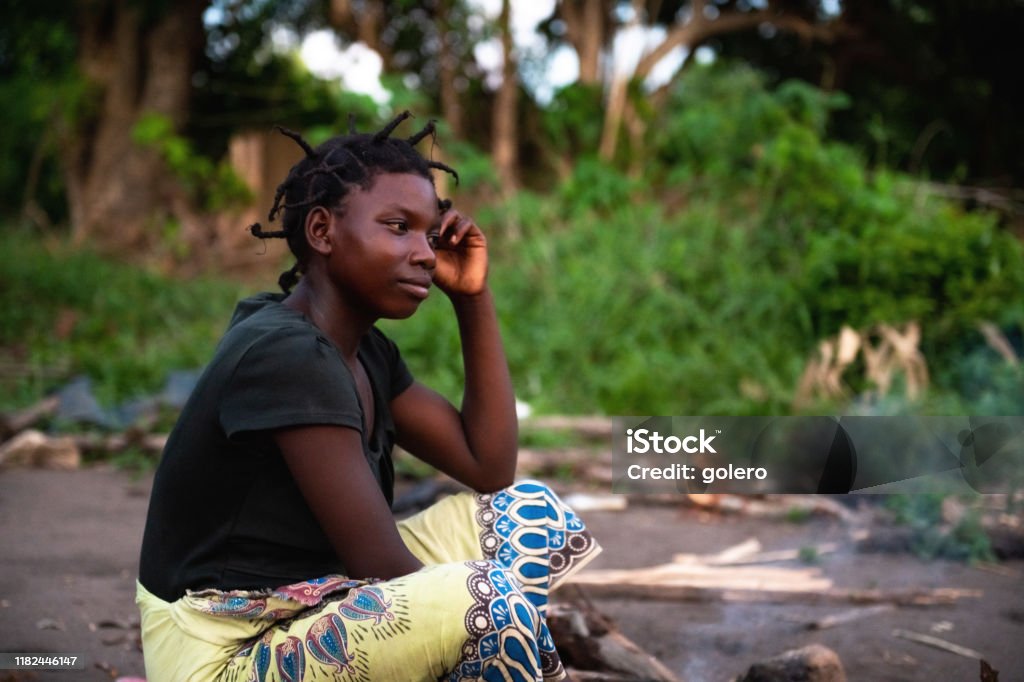 portait of young african woman sitting on the ground portait of young african woman sitting on the ground in village in Malawi Malawi Stock Photo
