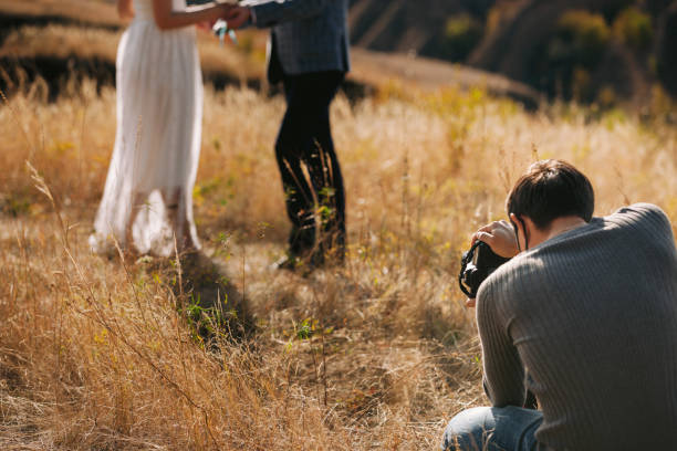 wedding photographer takes pictures of the bride and groom wedding photographer takes pictures of couple in nature in autumn, the photographer in action wedding photos stock pictures, royalty-free photos & images