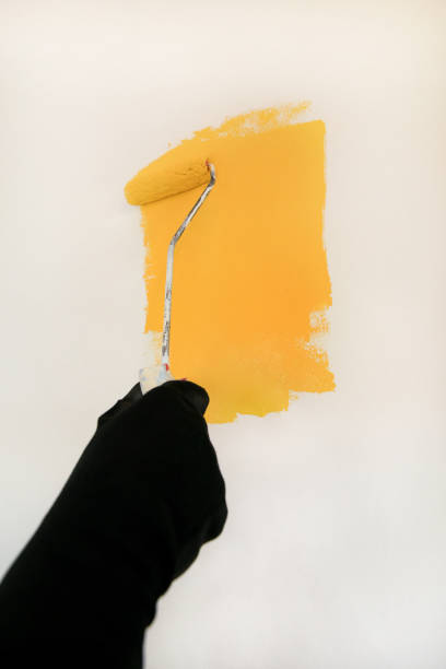 istock Construction worker and handyman doing finish renovation at apartment. Professional painter using paint roller brush painting of wall with yellow color on construction site. Home renovation concept. 1182449121