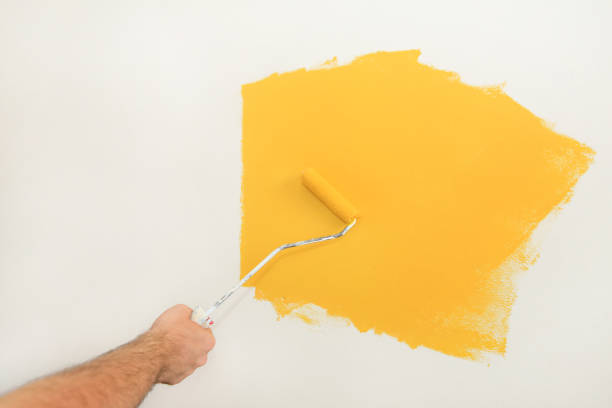 istock Construction worker and handyman doing finish renovation at apartment. Professional painter using paint roller brush painting of wall with yellow color on construction site. Home renovation concept. 1182449171