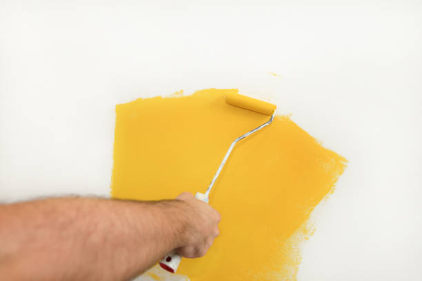 istock Construction worker and handyman doing finish renovation at apartment. Professional painter using paint roller brush painting of wall with yellow color on construction site. Home renovation concept. 1182449175