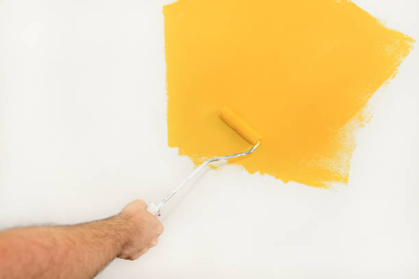 istock Construction worker and handyman doing finish renovation at apartment. Professional painter using paint roller brush painting of wall with yellow color on construction site. Home renovation concept. 1182449202