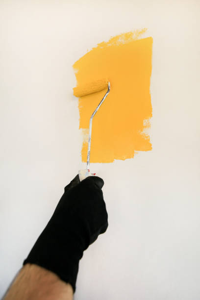 istock Construction worker and handyman doing finish renovation at apartment. Professional painter using paint roller brush painting of wall with yellow color on construction site. Home renovation concept. 1182449250