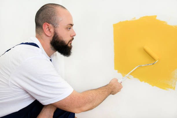 istock Construction worker and handyman doing finish renovation at apartment. Professional painter using paint roller brush painting of wall with yellow color on construction site. Home renovation concept. 1182449252