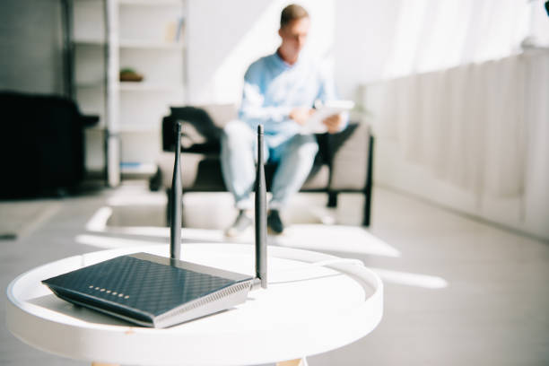 selective focus of black plugged router on white table and businessman sitting on sofa selective focus of black plugged router on white table and businessman sitting on sofa wireless technology stock pictures, royalty-free photos & images