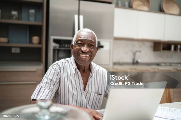 Portrait Of A Senior Man Using Laptop In The Kitchen Table Stock Photo - Download Image Now