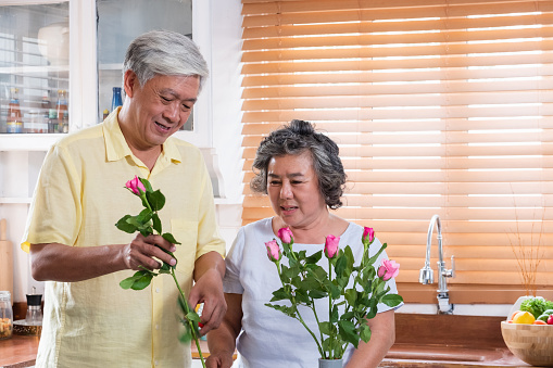 Asian Senior couple husband and wife flower arrangement to vase on table in kitchen at home in Valentine's Day.lovely senior couple concept