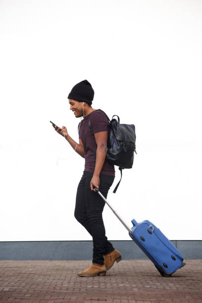 côté de corps complet de l'homme américain africain marchant avec des bagages et le téléphone portable par le mur blanc - pulling a name from a hat photos et images de collection