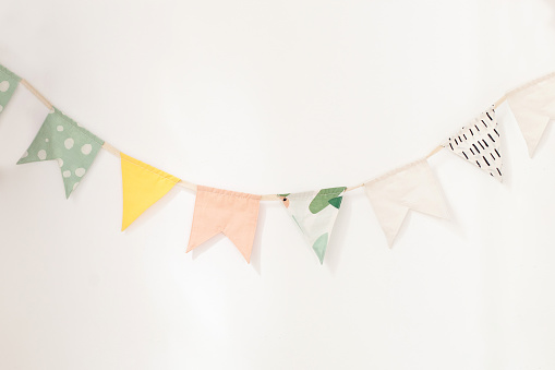 wall is decorated with multi-colored flags for children. Birthday decor decoration flags. Decor for the holiday.\nparty flags hanging on white background, decorate items for festival, celebrate event